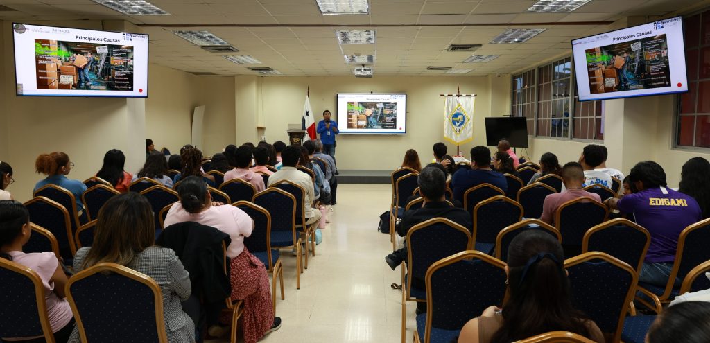jornada de seguridad UTP 2026: representante del MITRADEL impartiendo la conferencia sobre accidentes laborales, inspecciones y cumplimiento normativo ante un auditorio lleno de estudiantes en el Salón Cardoze de la Facultad de Ingeniería Industrial de la UTP.